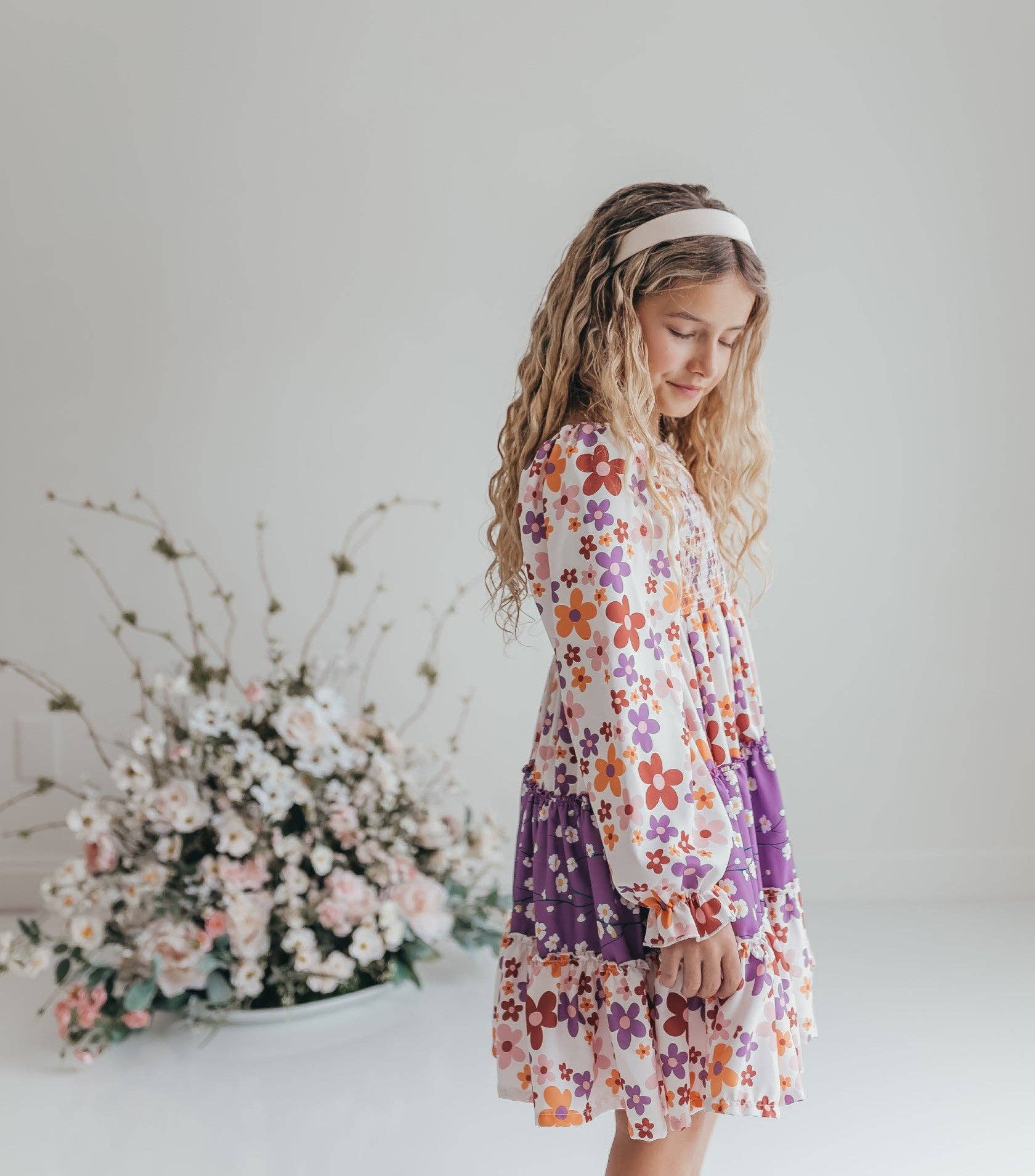 Young girl in a floral dress standing next to a flower arrangement on a white background