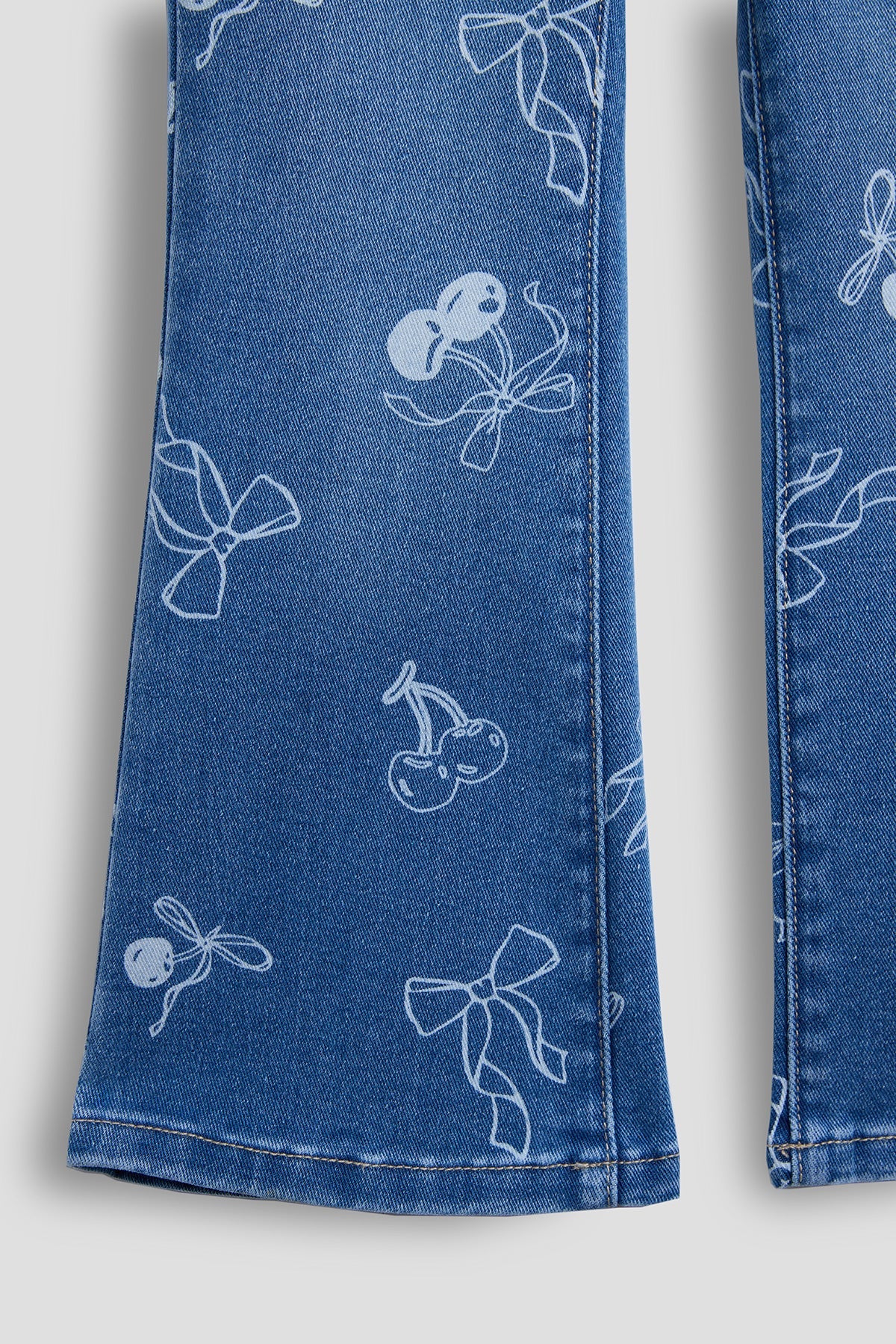 Close-up of blue denim jeans with white bow and cherry patterns on a light gray background