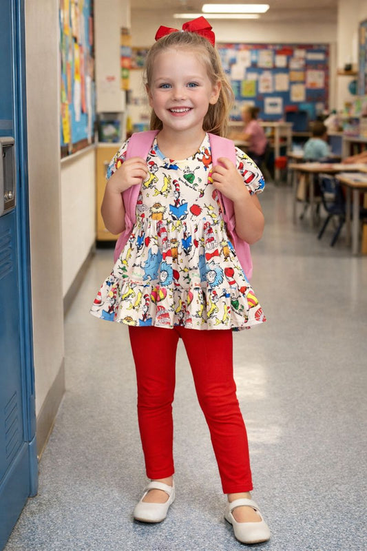 Young girl in a classroom wearing a colorful dress and red leggings with a pink backpack.