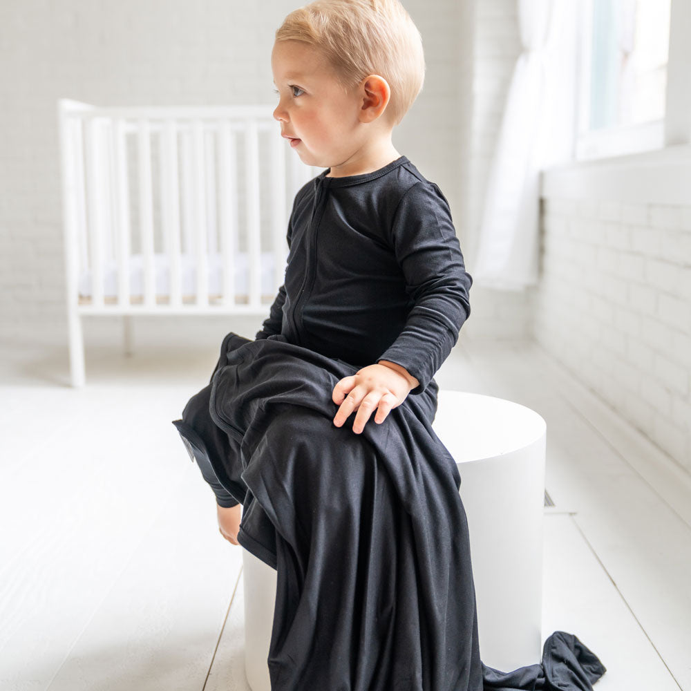 Child wearing a black outfit sitting on a white stool in a bright room.