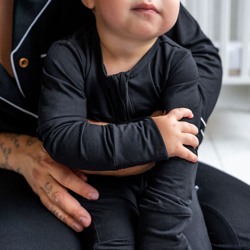 Child wearing a black outfit sitting on an adult's lap indoors.