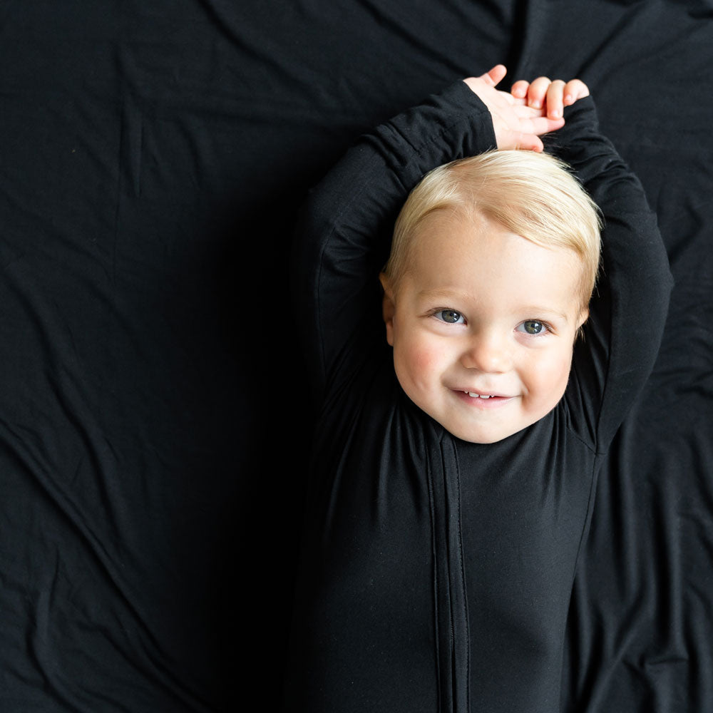 Child wearing a black outfit with arms raised against a black background