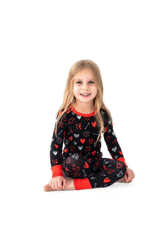 A child sitting and smiling, wearing a red and black heart-patterned pajama set.