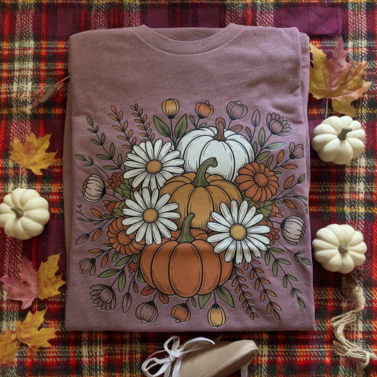 Purple t-shirt with autumn-themed design featuring pumpkins and flowers on a plaid fabric background.