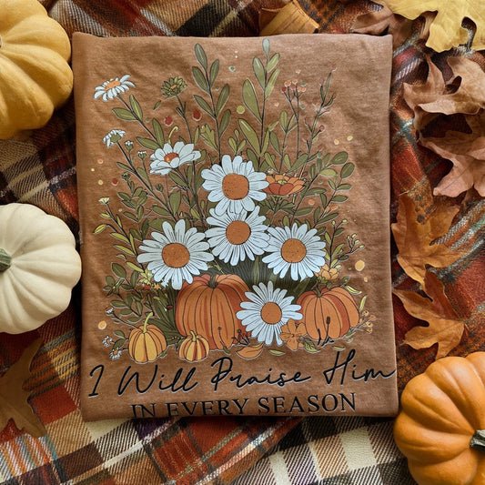 Decorative pillow with floral and pumpkin design on a plaid fabric background with pumpkins and leaves.