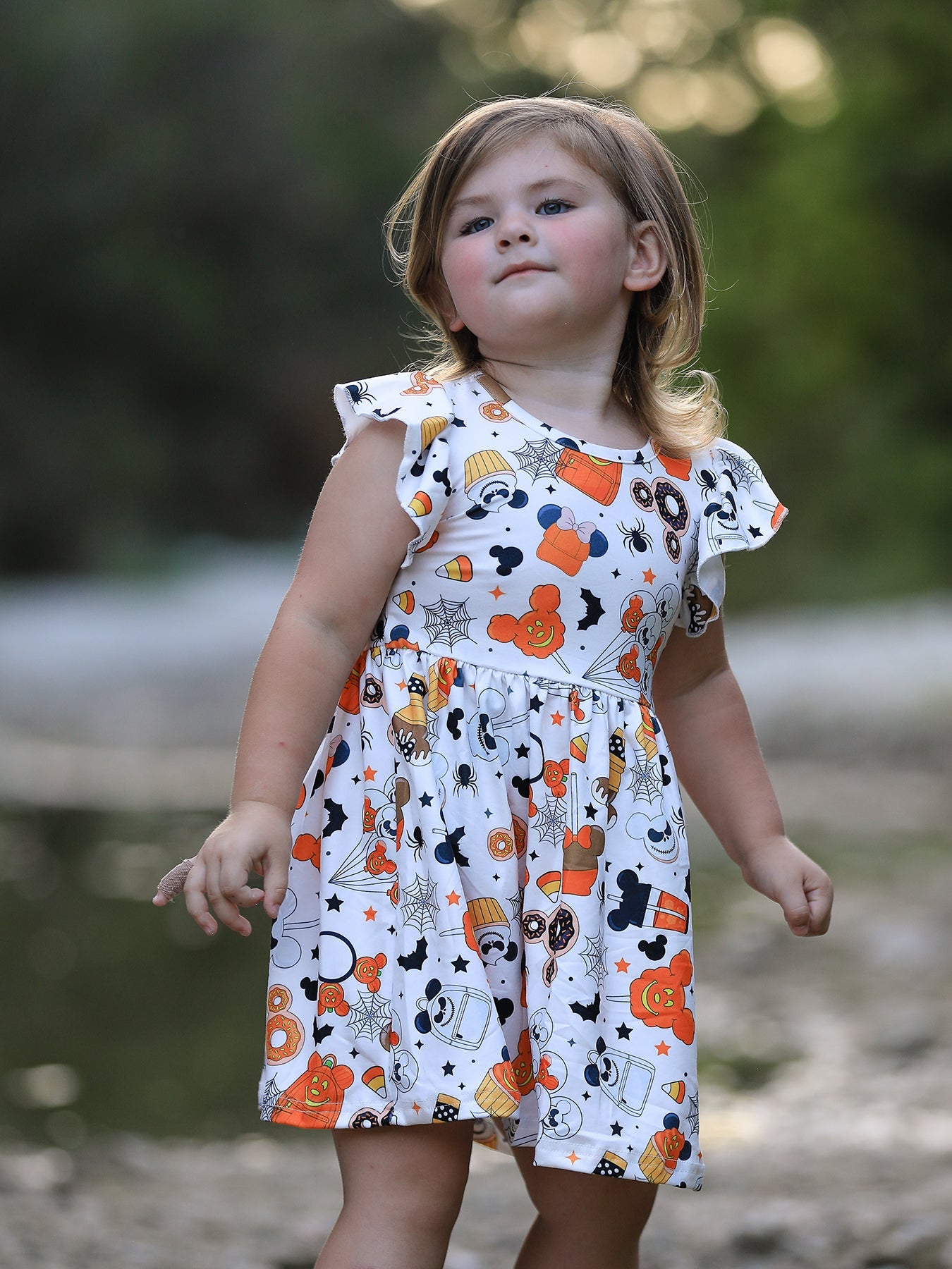 Young girl wearing a Halloween-themed dress with pumpkins and ghosts outdoors.