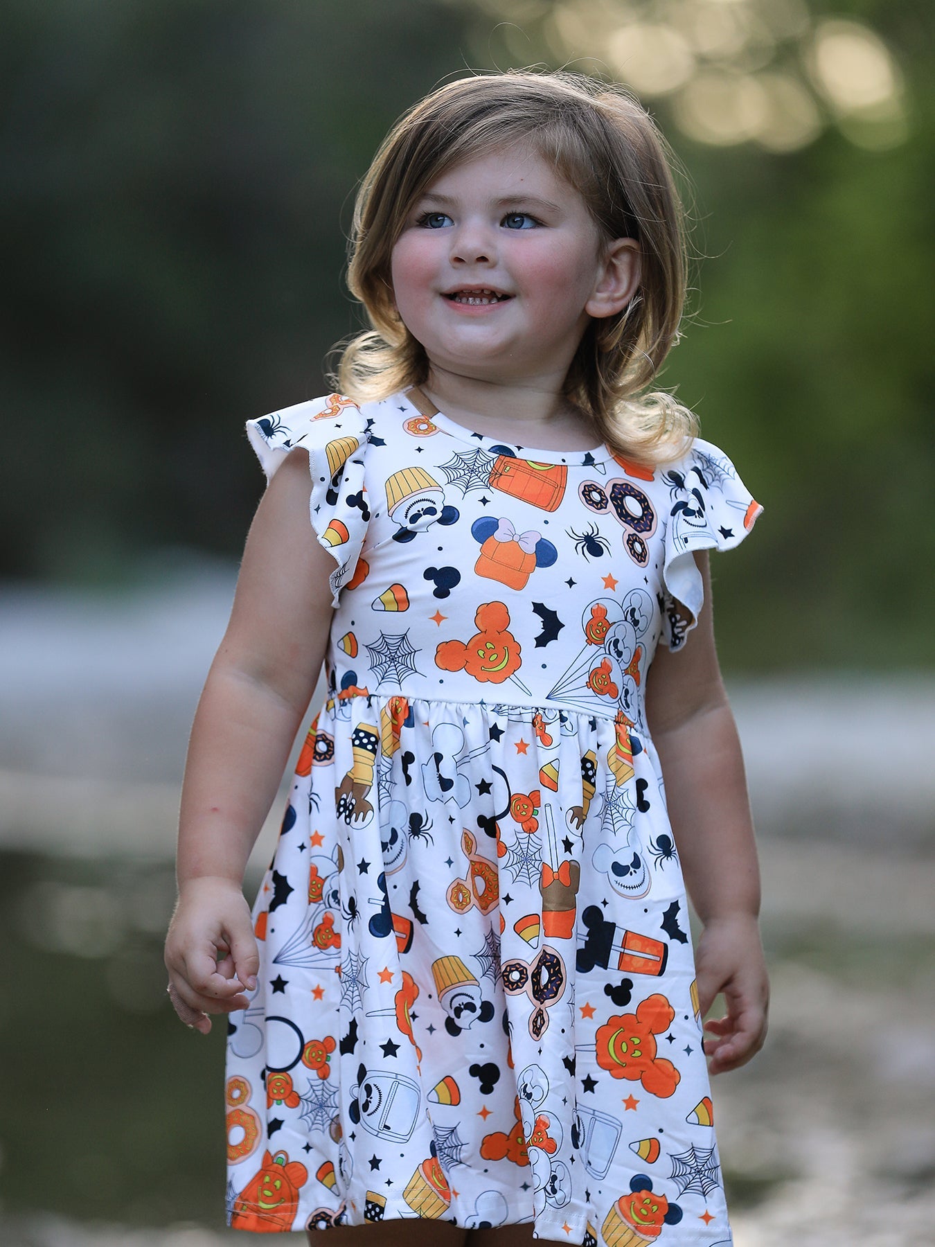 Young girl wearing a dress with Halloween-themed pattern outdoors
