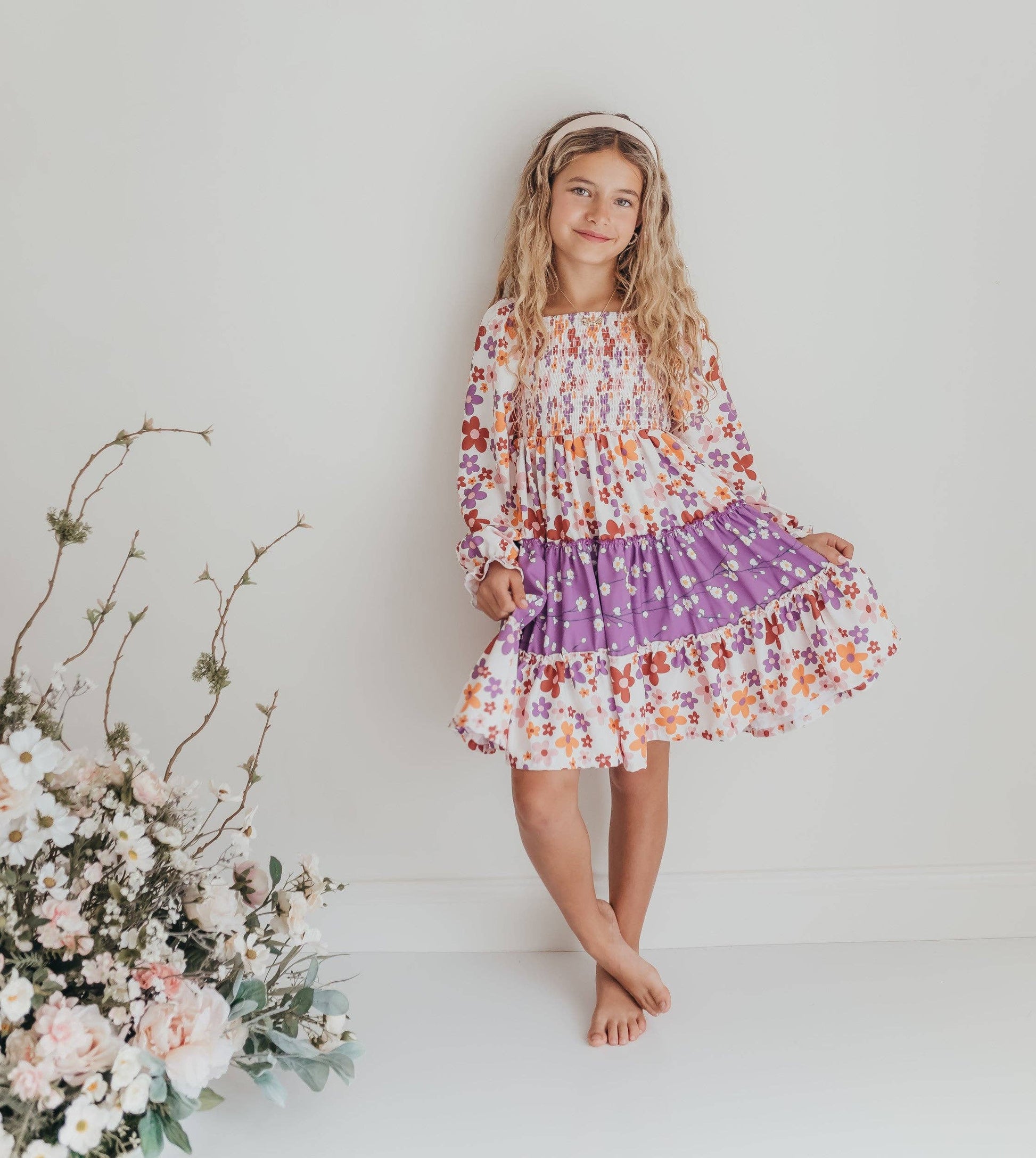 Young girl in a floral dress standing next to flowers on a white background