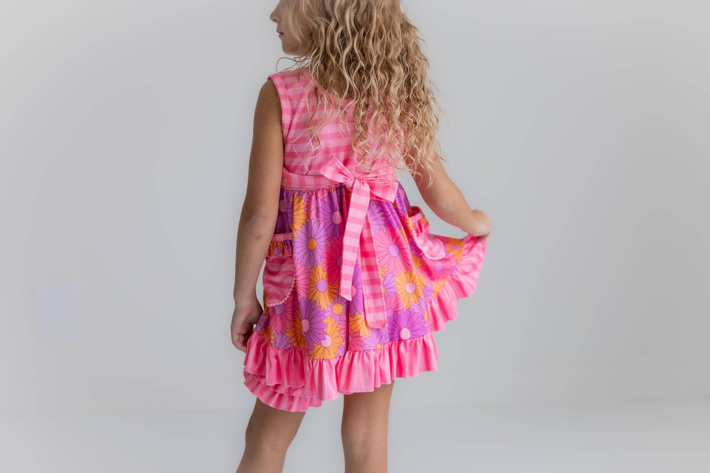 Child wearing a pink dress with floral patterns on a plain background