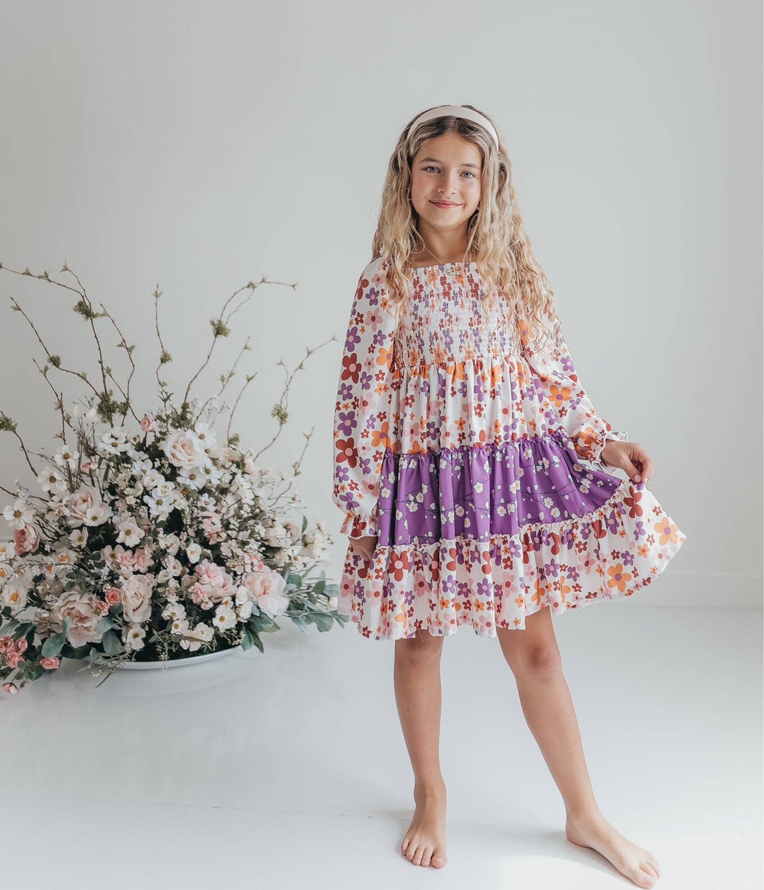 Young girl in a floral dress standing next to a floral arrangement on a white background