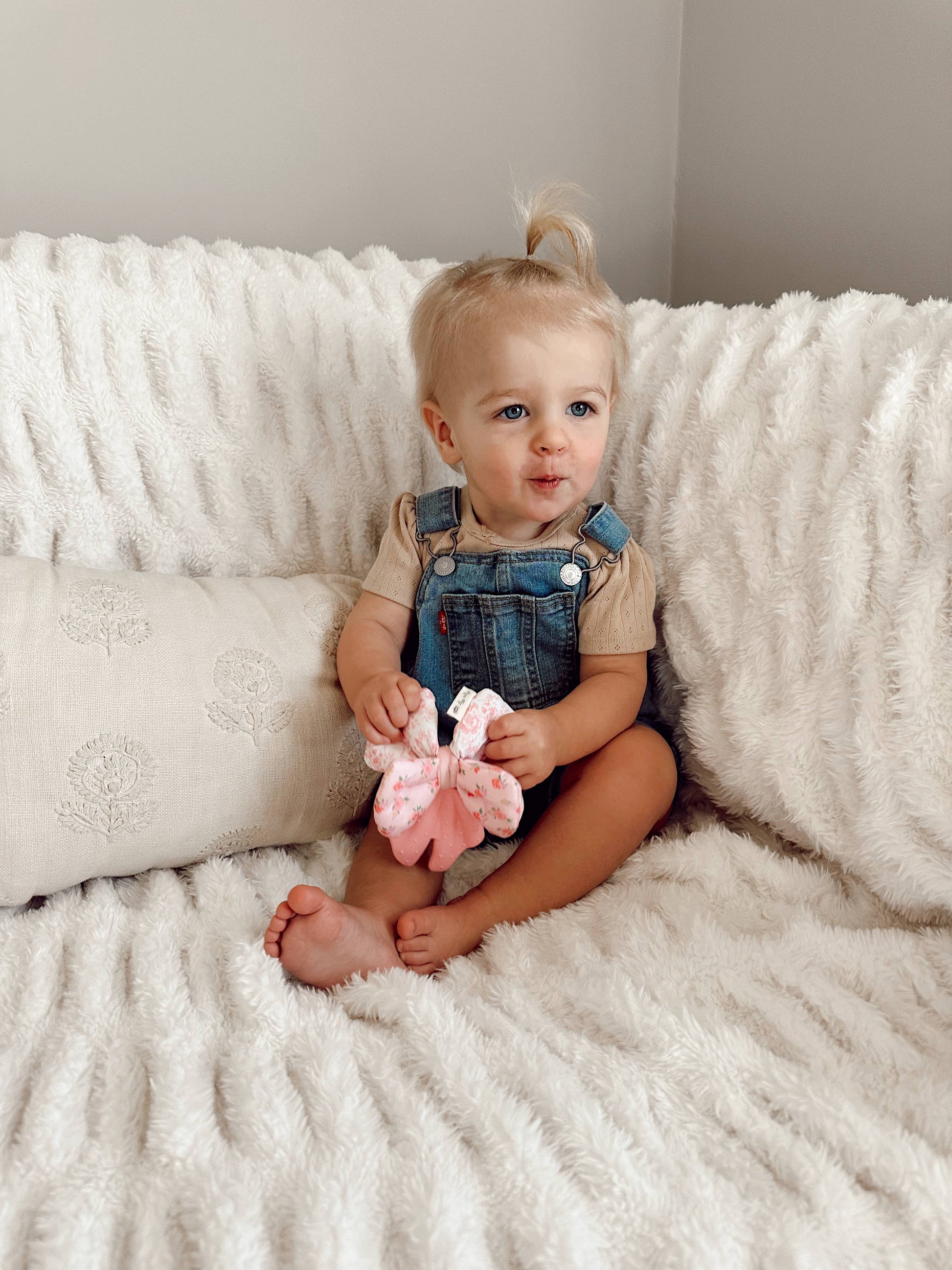 Child sitting on a white couch holding a pink toy