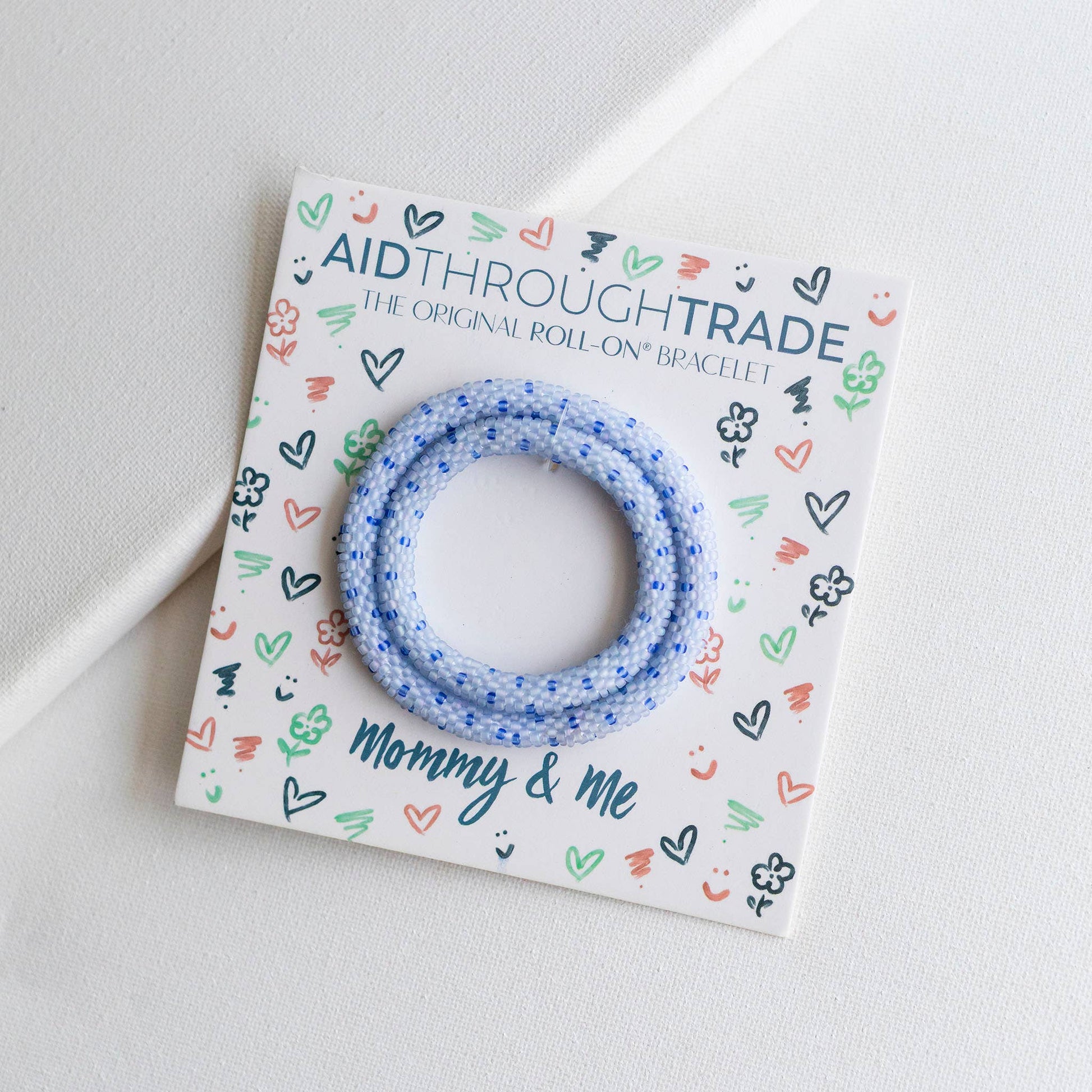 Blue bracelet on a colorful 'Aid Through Trade' card with 'Mommy & Me' text on a light gray background