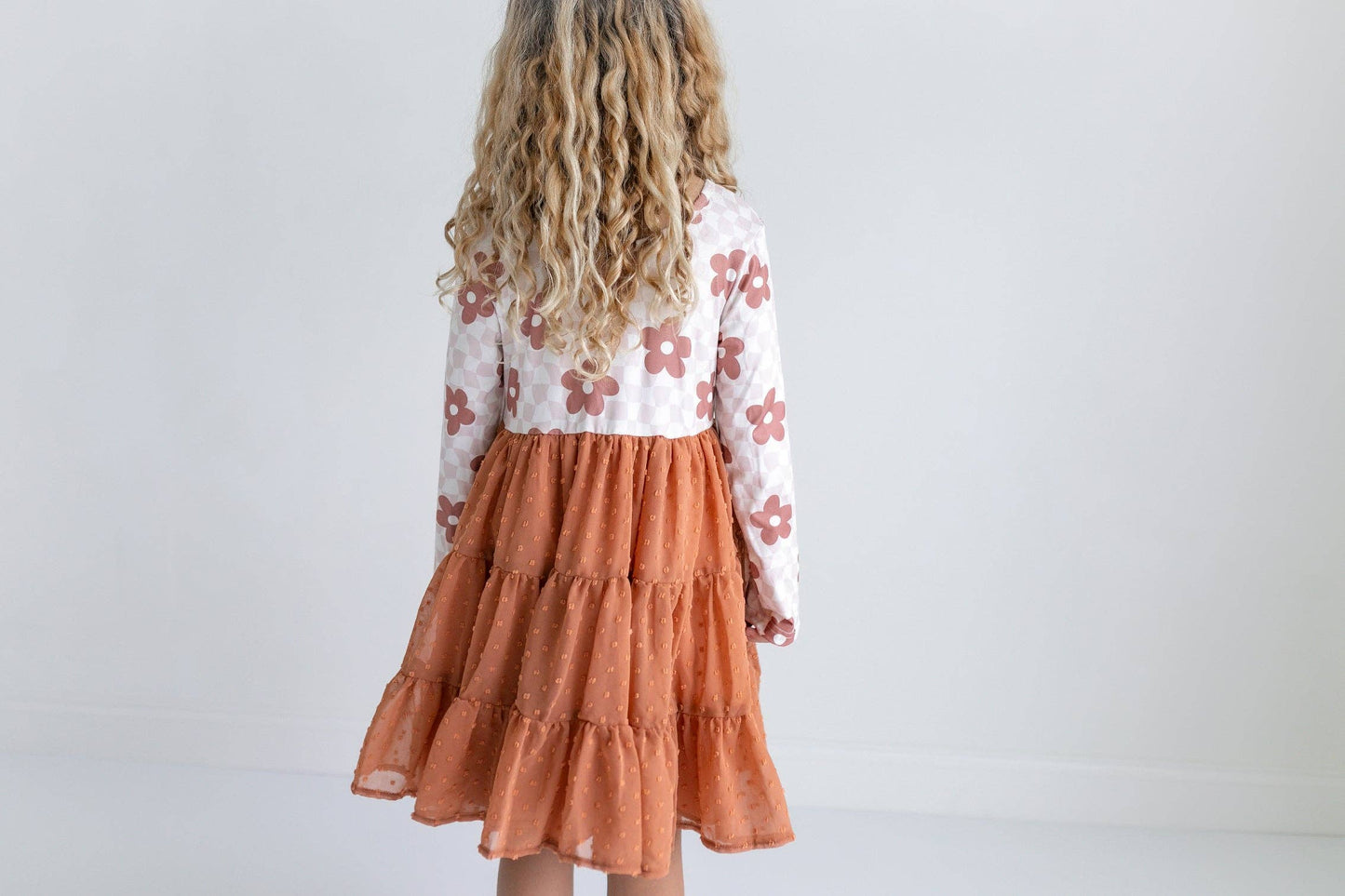 Child wearing a floral long-sleeve dress with a tiered rust-colored skirt against a white background