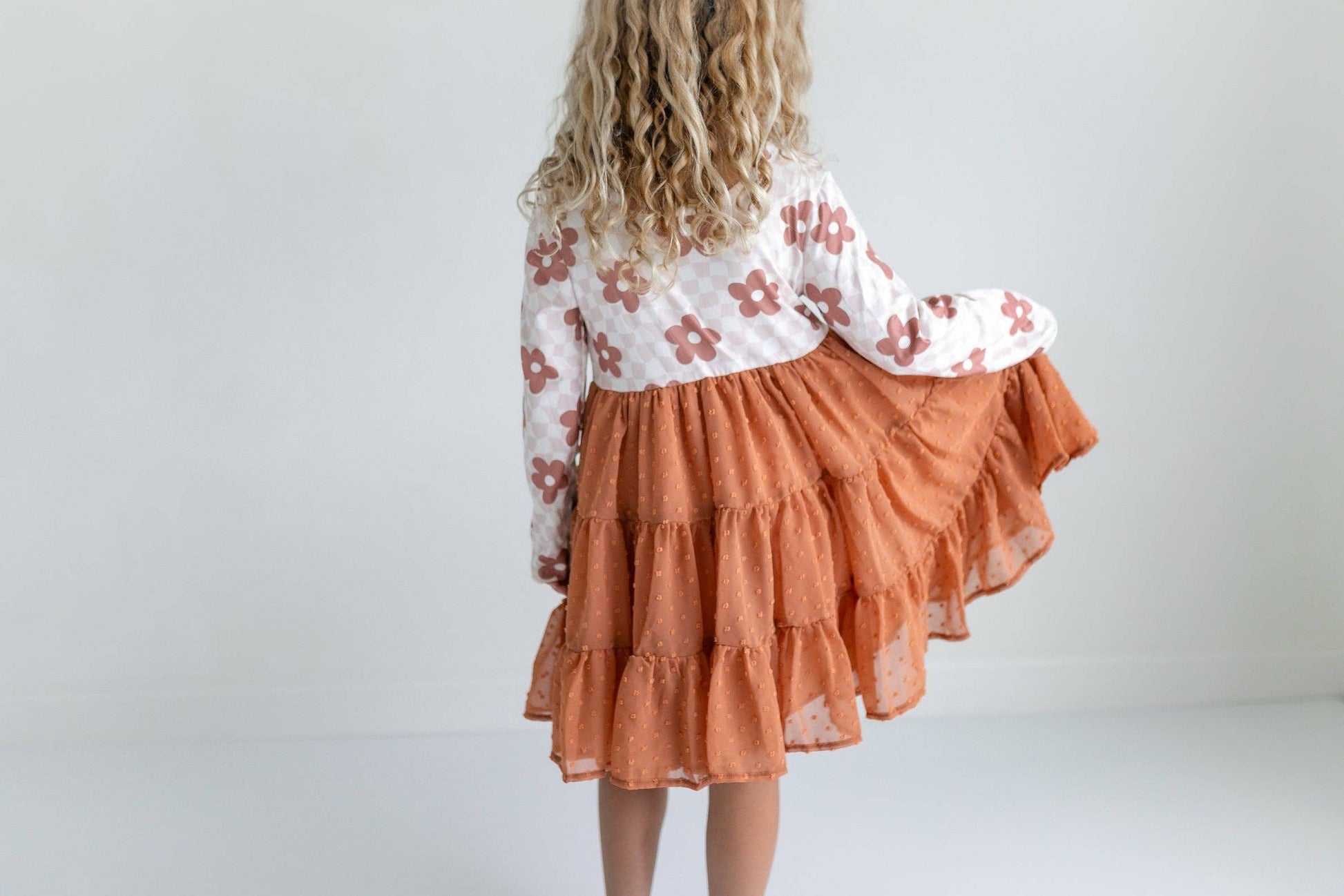 Child wearing a floral top and orange skirt against a white background