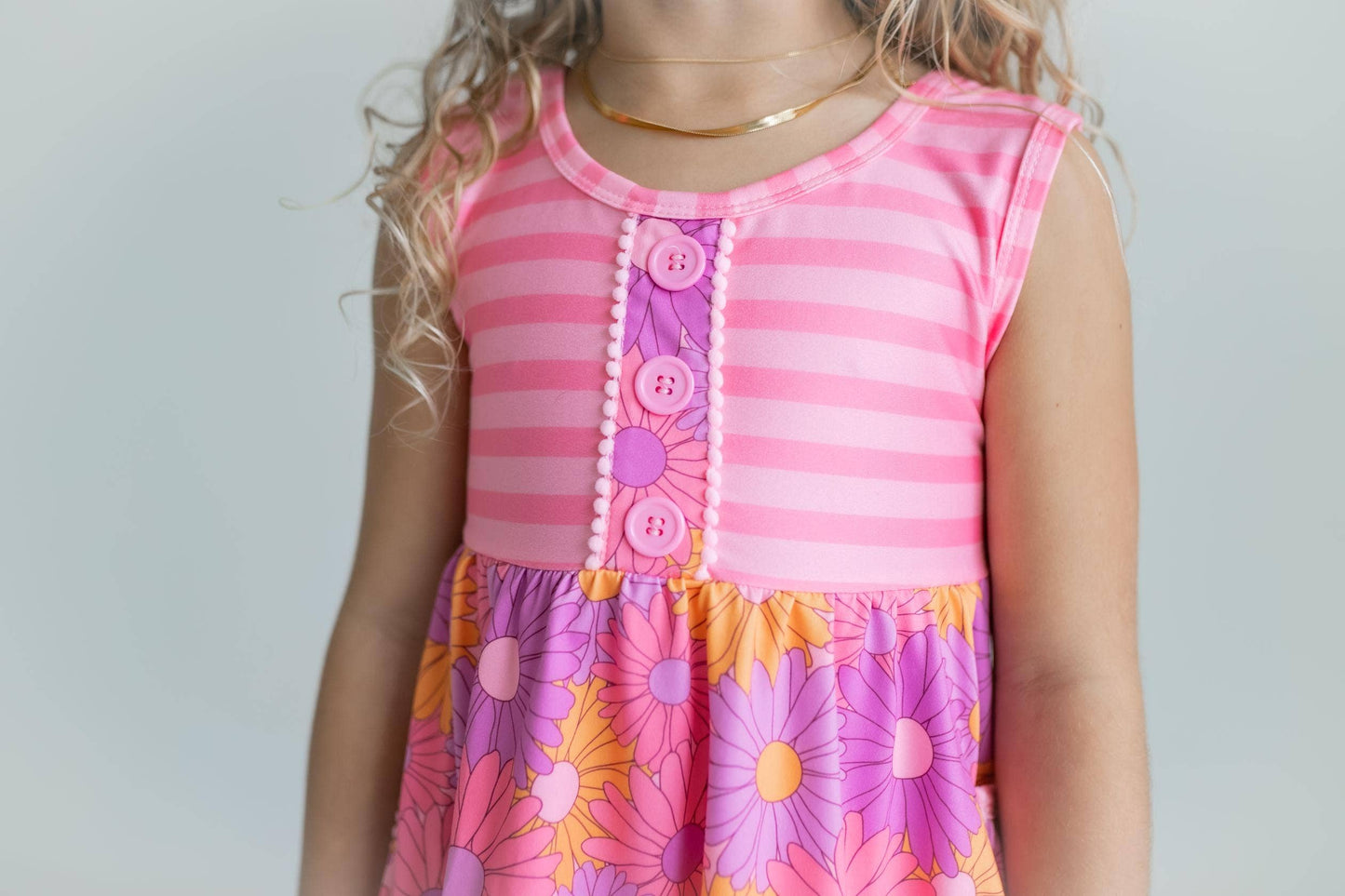 Child wearing a pink and purple striped dress with a floral skirt against a plain background