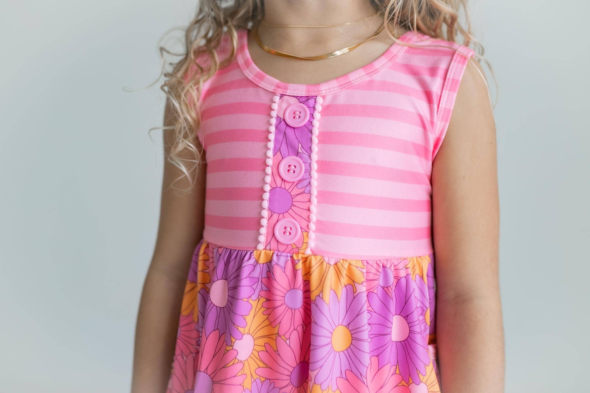 Child wearing a pink and purple striped dress with a floral skirt against a plain background
