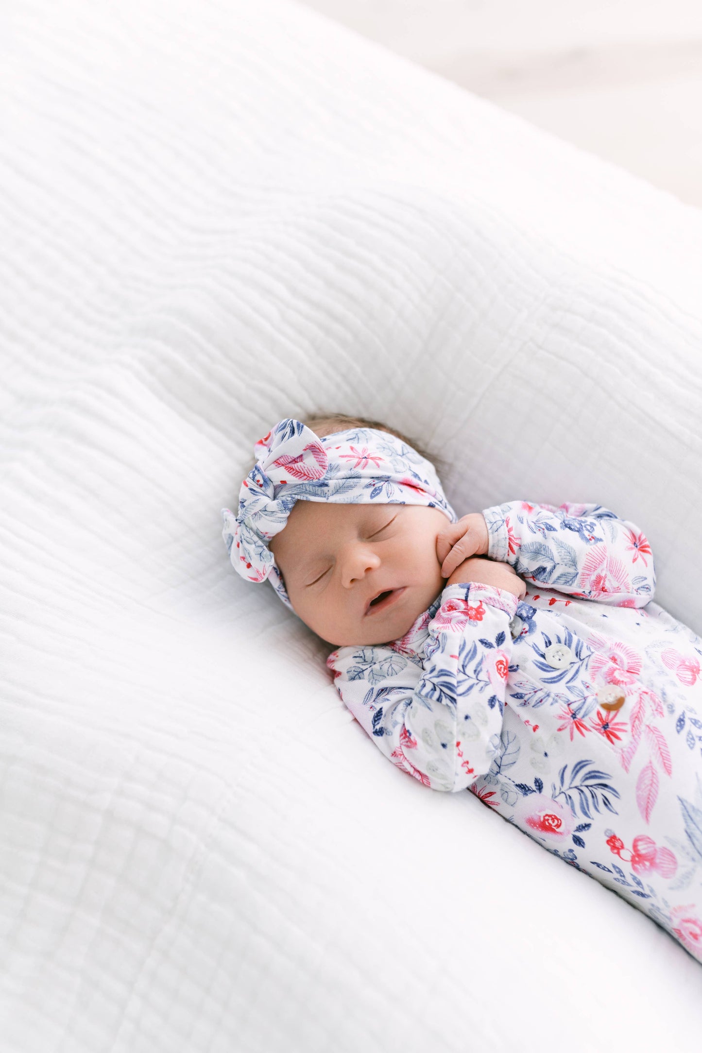 Newborn baby swaddled in a floral outfit with a matching headband on a white background