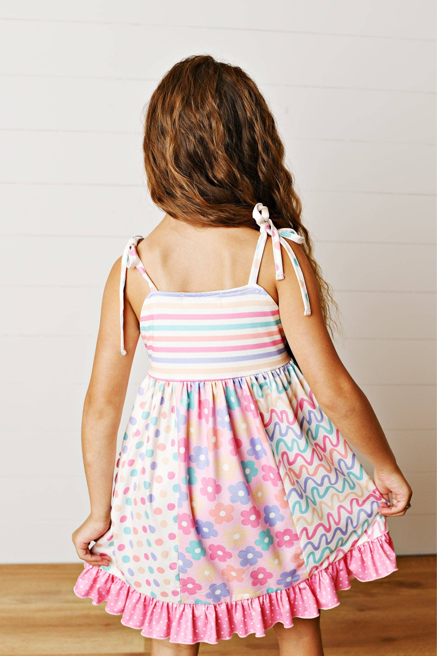 Young girl wearing a colorful dress with floral patterns and pink ruffle trim.