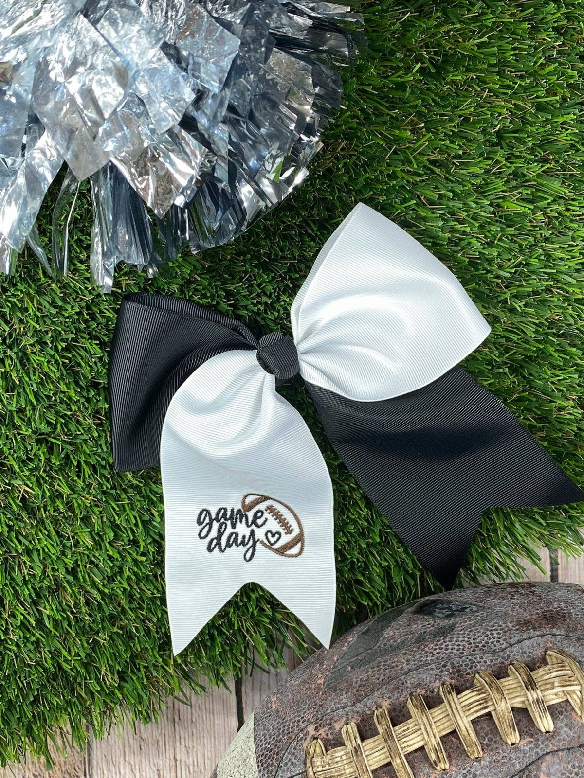 Black and White cheer bow with 'game day' embroidered. Shown on faux grass with silver pom poms & a football. 