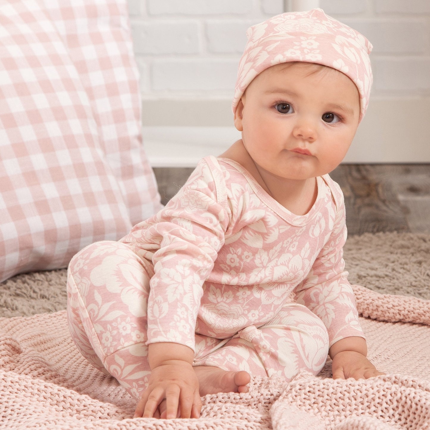 Baby in pink floral outfit sitting on a soft surface