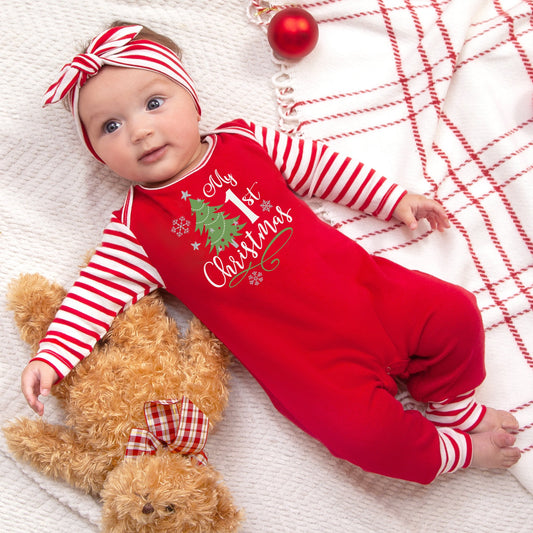 Baby in a red and white Christmas-themed outfit lying on a blanket with a teddy bear.
