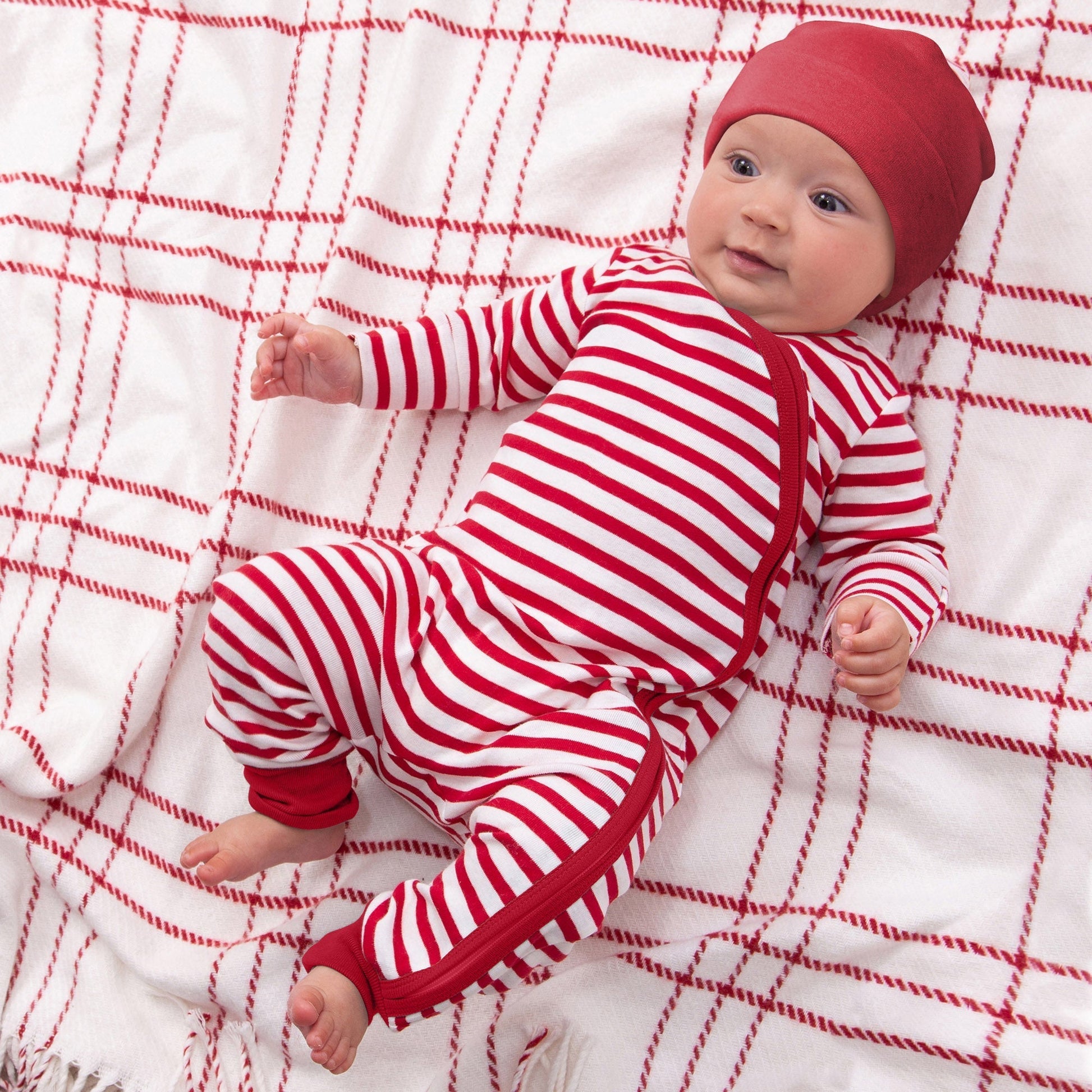 Baby in red and white striped outfit lying on a red and white checkered blanket